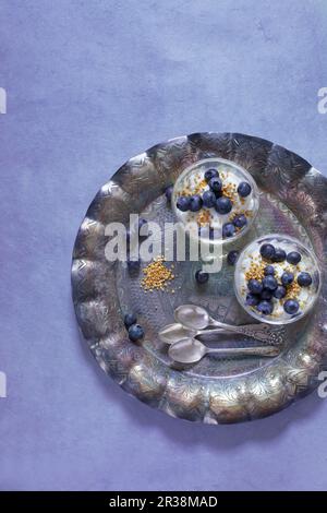 Zwei Glasschüsseln reinen Joghurt mit Blaubeeren und Bienenpollen auf einem Silbertablett Stockfoto