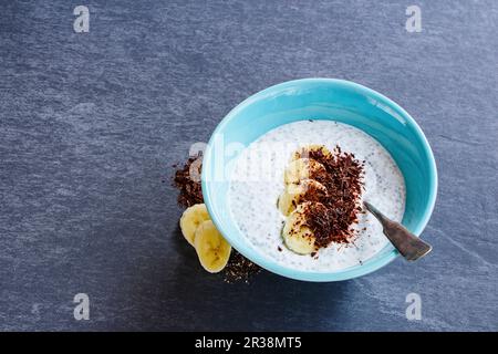 Frühstück Mandelmilch Chiasamen Pudding mit Banane und Schokolade in der Schüssel auf grauem Steinhintergrund Stockfoto