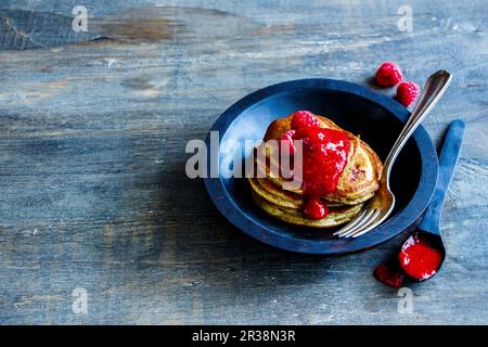 Nahaufnahme von frisch zubereiteten Pfannkuchen mit Himbeermarmelade und frischen Himbeeren in rustikaler Holzschüssel zum Frühstück Stockfoto