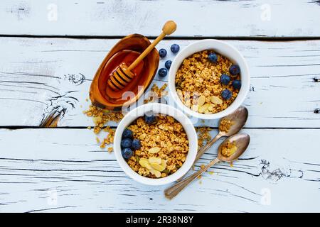 Top View mit köstlichem Müsli und gesunden Frühstückszutaten - Honig, frische Blaubeeren und Nüsse auf weißem Grunge Hintergrund Stockfoto