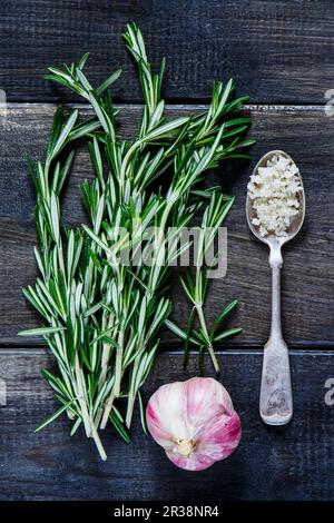 Meersalz in altem Metalllöffel, Knoblauch und Rosmarin auf dunklem Holzbrett Stockfoto
