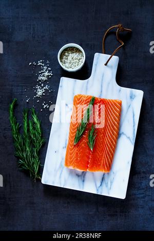 Frisches, rohes Lachsfilet mit Rosmarin und grauem Salz auf dem Schneidebrett Stockfoto