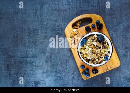 Blick von oben auf den köstlichen Frühstückstisch mit Granola in klassischer Schüssel und frischen dunklen Beeren auf Grunge-Hintergrund Stockfoto