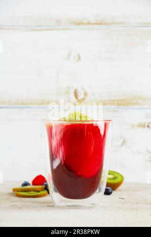 Glas aus dreifarbigem Frucht-Smoothie mit frischen Beeren und Früchten, weißer Holzhintergrund Stockfoto