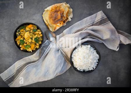 Gemüse-Curry mit Blumenkohl, Butternusskürbis, Spinat und Koriander, serviert mit Papadomen und Reis Stockfoto