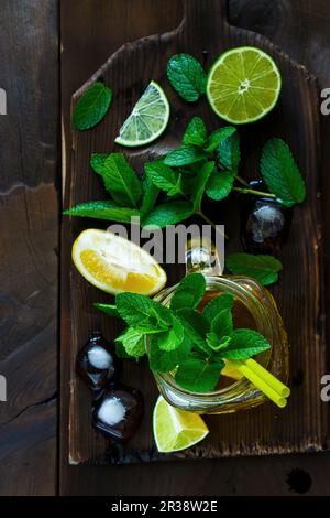 Grüner Tee mit Limette, Zitrone und Minze in einer Glaskanne auf einem Holzbrett Stockfoto