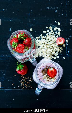 Roter ErdbeerSmoothie mit Chiasamen und Haferflocken im Glas, serviert mit frischen Erdbeeren vor dunklem Hintergrund Stockfoto