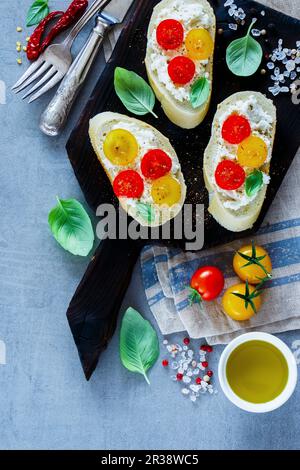 Nahaufnahme von hausgemachten Tomaten- und Basilikum-Bruschetta oder Sandwiches mit Zutaten auf hellgrauem Hintergrund Stockfoto