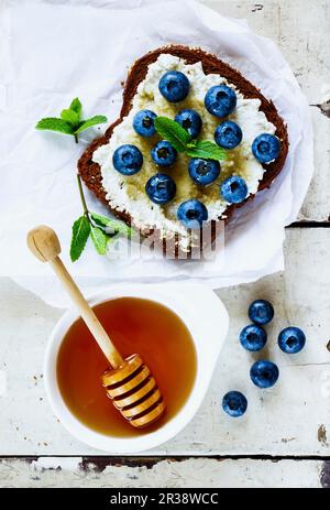 Nahaufnahme des Grunge weißen Holztischs mit Ricotta, frischen Blaubeeren und Honigsandwich auf Vollkornbrot Stockfoto