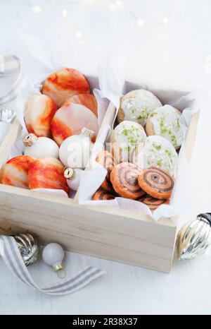 Orangefarbene Kekse mit Marmororangenguss, orangefarbene und Schokoladenkekse sowie Limonen- und Kokosbrotkekse in einer hölzernen Geschenkbox wi Stockfoto