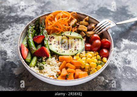 Eine Buddha-Schüssel mit Bulgur, grünem Spargel, Erdbeeren, Karotten, Tofu, Tomaten, Zuckermais, Süßkartoffeln und Avocado Stockfoto