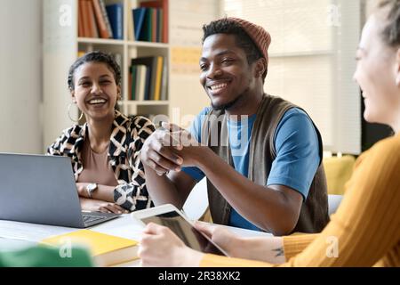 Gruppe multiethnischer Schüler, die lachen, während sie am Tisch sitzen und während des Unterrichts im Team arbeiten Stockfoto