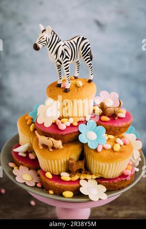 Cupcakes auf einem Kuchenständer, der mit Tierfiguren, Blumen und Süßigkeiten geschmückt ist Stockfoto