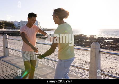 Glückliches birassisches, schwules Paar, das Spaß hat, auf der Promenade am Meer zu tanzen Stockfoto