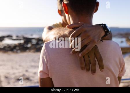 Rückansicht eines glücklichen, birassischen, homosexuellen Paares, das sich am Meer umarmt Stockfoto