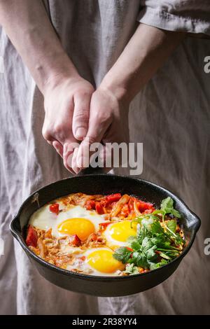 Traditionelle israelische Küche Gerichte Shakshuka (Gebratene Eier mit Gemüsestomaten und Paprika in gusseiserner Pfanne in weiblichen Händen) Stockfoto