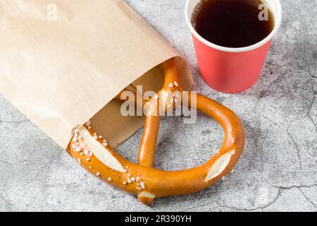 Brezel in Geschenkpapier eingewickelt mit einem Getränk daneben auf einem Steintisch Stockfoto