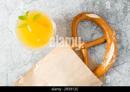 Brezel in Geschenkpapier eingewickelt mit einem Getränk daneben auf einem Steintisch Stockfoto