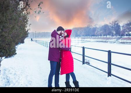 Ein junges Paar, das sich während des Winterspaziergangs in der Stadt umarmt Stockfoto