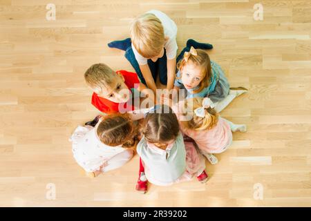 Sechs Kinder sitzen im Kreis mit den Händen zusammen Stockfoto