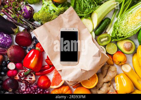 Regenbogenfarbenes Obst und Gemüse auf dem Tisch und Smartphone Stockfoto