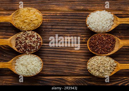 Holzlöffel mit verschiedenen Reissorten auf dem Holzhintergrund Stockfoto