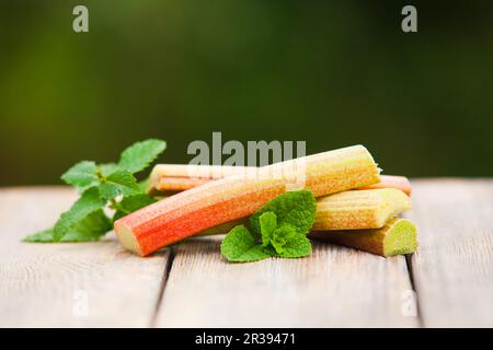 Frischer Rhabarber mit Minzblättern auf einem Holztisch Stockfoto