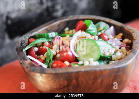 Israelischer Couscous-Salat mit Gurken, Tomaten und frischem Basilikum in einer Holzschüssel Stockfoto