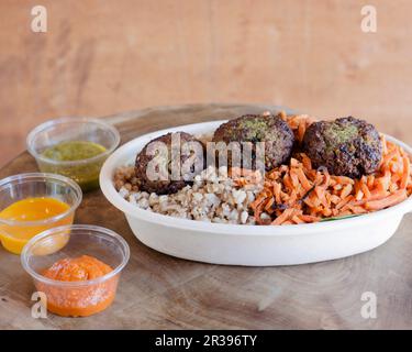 Eine Falafel-Schüssel mit Gemüse und drei Dips Stockfoto