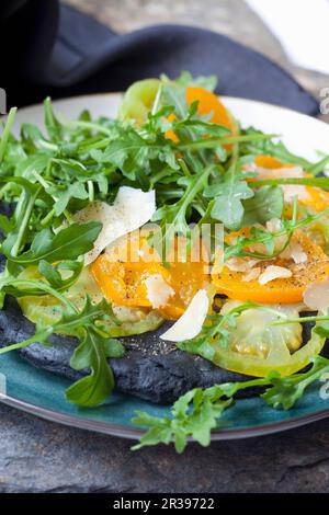 Schwarze Pizza mit Aktivkohle, grünen und gelben Tomaten, Parmesankäse und Rucola Stockfoto