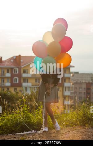Mädchen mit bunten Ballons bleiben bei Sonnenuntergang Stockfoto