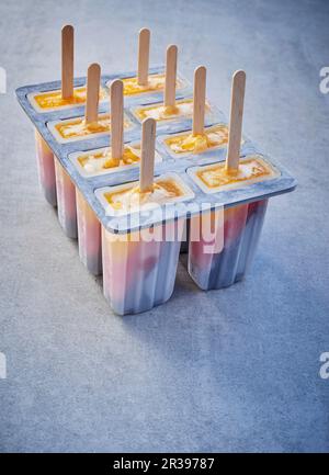 Dreifarbige Eisstäbchen in Lolly-Schimmelpilzen auf einer grauen Oberfläche Stockfoto