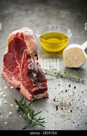 Rohes Porterhouse-Steak mit Kräuterzweigen, Pfeffer, Meersalz, Knoblauch und Olivenöl Stockfoto