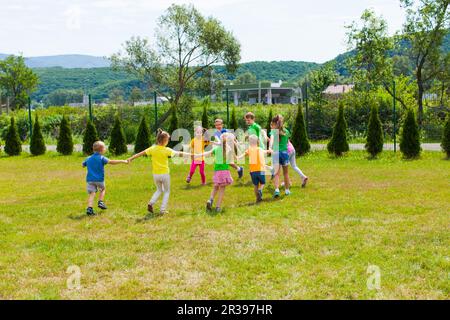 Kinder Rennen und halten sich auf dem grünen Rasen an den Händen Stockfoto