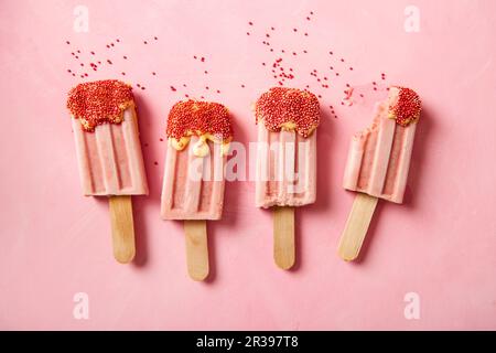 Erdbeer-Eiscreme-Lollies mit Zuckerstreuseln, einer mit einem Bissen herausgenommen Stockfoto