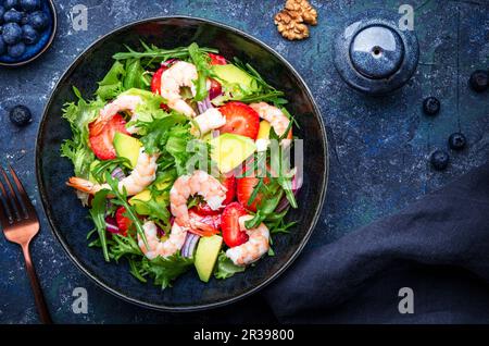 Leckerer Salat mit frischen Erdbeeren, Garnelen, Rucola, Avocado und roten Zwiebeln, blauem Steintisch. Frisches, nützliches Gericht für gesunde Ernährung Stockfoto