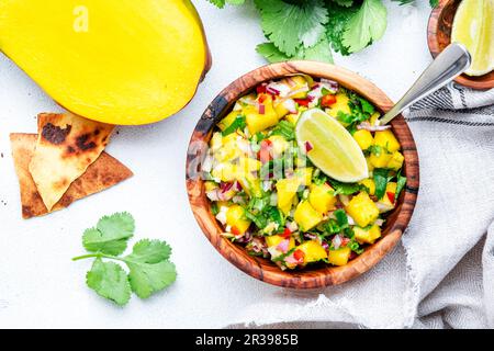 Mango Salsa – scharfe Sauce mit Chili-Paprika, Zwiebeln, Knoblauch, Limette und Koriander in einer Holzschüssel auf weißem Tischhintergrund, Draufsicht Stockfoto