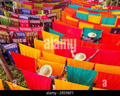 Narayanganj, Dhaka, Bangladesch. 23. Mai 2023, Narayanganj, Dhaka, Bangladesch: Arbeiter hängen Hunderte von farbigen Stoffblättern auf ein Bambusgerüst, um sie in einer Färbefabrik in Narayanganj, Bangladesch, zu trocknen. Der Trocknungsvorgang dauert in der Regel 4 Stunden, wobei jeder Satz aus jeweils 200 Teilen besteht, um bei Temperaturen über 42 °C zu trocknen. Arbeiter verwenden Hüte zum Schutz vor der brennenden Hitze, da sie die bunten Stoffe ständig drehen müssen, damit sie im Sonnenlicht perfekt trocknen. Kredit: ZUMA Press, Inc./Alamy Live News Stockfoto