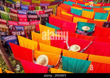 Narayanganj, Dhaka, Bangladesch. 23. Mai 2023, Narayanganj, Dhaka, Bangladesch: Arbeiter hängen Hunderte von farbigen Stoffblättern auf ein Bambusgerüst, um sie in einer Färbefabrik in Narayanganj, Bangladesch, zu trocknen. Der Trocknungsvorgang dauert in der Regel 4 Stunden, wobei jeder Satz aus jeweils 200 Teilen besteht, um bei Temperaturen über 42 °C zu trocknen. Arbeiter verwenden Hüte zum Schutz vor der brennenden Hitze, da sie die bunten Stoffe ständig drehen müssen, damit sie im Sonnenlicht perfekt trocknen. Kredit: ZUMA Press, Inc./Alamy Live News Stockfoto