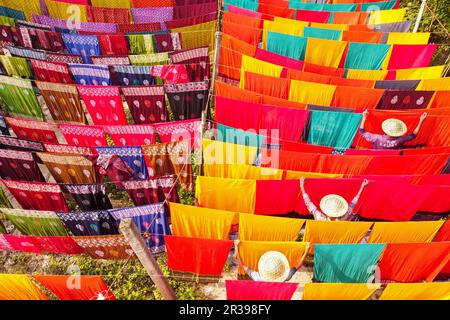 Narayanganj, Dhaka, Bangladesch. 23. Mai 2023, Narayanganj, Dhaka, Bangladesch: Arbeiter hängen Hunderte von farbigen Stoffblättern auf ein Bambusgerüst, um sie in einer Färbefabrik in Narayanganj, Bangladesch, zu trocknen. Der Trocknungsvorgang dauert in der Regel 4 Stunden, wobei jeder Satz aus jeweils 200 Teilen besteht, um bei Temperaturen über 42 °C zu trocknen. Arbeiter verwenden Hüte zum Schutz vor der brennenden Hitze, da sie die bunten Stoffe ständig drehen müssen, damit sie im Sonnenlicht perfekt trocknen. Kredit: ZUMA Press, Inc./Alamy Live News Stockfoto