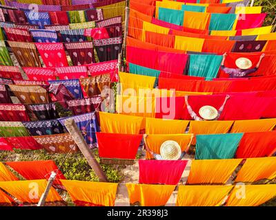 Narayanganj, Dhaka, Bangladesch. 23. Mai 2023, Narayanganj, Dhaka, Bangladesch: Arbeiter hängen Hunderte von farbigen Stoffblättern auf ein Bambusgerüst, um sie in einer Färbefabrik in Narayanganj, Bangladesch, zu trocknen. Der Trocknungsvorgang dauert in der Regel 4 Stunden, wobei jeder Satz aus jeweils 200 Teilen besteht, um bei Temperaturen über 42 °C zu trocknen. Arbeiter verwenden Hüte zum Schutz vor der brennenden Hitze, da sie die bunten Stoffe ständig drehen müssen, damit sie im Sonnenlicht perfekt trocknen. Kredit: ZUMA Press, Inc./Alamy Live News Stockfoto