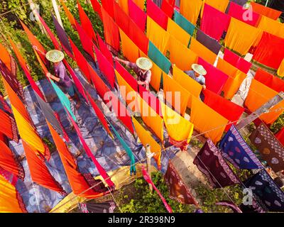 Narayanganj, Dhaka, Bangladesch. 23. Mai 2023, Narayanganj, Dhaka, Bangladesch: Arbeiter hängen Hunderte von farbigen Stoffblättern auf ein Bambusgerüst, um sie in einer Färbefabrik in Narayanganj, Bangladesch, zu trocknen. Der Trocknungsvorgang dauert in der Regel 4 Stunden, wobei jeder Satz aus jeweils 200 Teilen besteht, um bei Temperaturen über 42 °C zu trocknen. Arbeiter verwenden Hüte zum Schutz vor der brennenden Hitze, da sie die bunten Stoffe ständig drehen müssen, damit sie im Sonnenlicht perfekt trocknen. Kredit: ZUMA Press, Inc./Alamy Live News Stockfoto