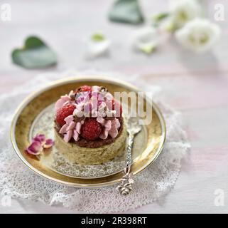 Veganer Zucchini-Kuchen mit Schokoladenganache, Himbeer-Mousse, frischen Himbeeren, Schokoladenlocken und getrockneten Rosenblättern Stockfoto