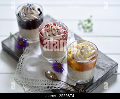 Vegane Reispudding Desserts in Gläsern mit Aprikosen-Mango, Himbeeren-Rhabarber und Blaubeersauce, dekoriert mit Kokosnusscreme und Blumen Stockfoto