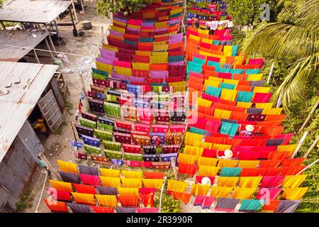 Narayanganj, Dhaka, Bangladesch. 23. Mai 2023, Narayanganj, Dhaka, Bangladesch: Arbeiter hängen Hunderte von farbigen Stoffblättern auf ein Bambusgerüst, um sie in einer Färbefabrik in Narayanganj, Bangladesch, zu trocknen. Der Trocknungsvorgang dauert in der Regel 4 Stunden, wobei jeder Satz aus jeweils 200 Teilen besteht, um bei Temperaturen über 42 °C zu trocknen. Arbeiter verwenden Hüte zum Schutz vor der brennenden Hitze, da sie die bunten Stoffe ständig drehen müssen, damit sie im Sonnenlicht perfekt trocknen. Kredit: ZUMA Press, Inc./Alamy Live News Stockfoto