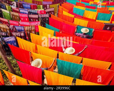 Narayanganj, Dhaka, Bangladesch. 23. Mai 2023, Narayanganj, Dhaka, Bangladesch: Arbeiter hängen Hunderte von farbigen Stoffblättern auf ein Bambusgerüst, um sie in einer Färbefabrik in Narayanganj, Bangladesch, zu trocknen. Der Trocknungsvorgang dauert in der Regel 4 Stunden, wobei jeder Satz aus jeweils 200 Teilen besteht, um bei Temperaturen über 42 °C zu trocknen. Arbeiter verwenden Hüte zum Schutz vor der brennenden Hitze, da sie die bunten Stoffe ständig drehen müssen, damit sie im Sonnenlicht perfekt trocknen. Kredit: ZUMA Press, Inc./Alamy Live News Stockfoto