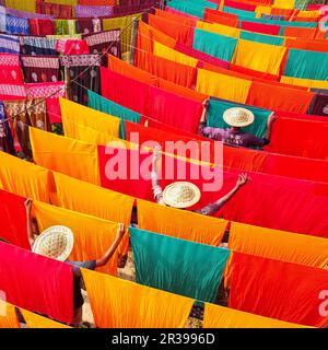 Narayanganj, Dhaka, Bangladesch. 23. Mai 2023, Narayanganj, Dhaka, Bangladesch: Arbeiter hängen Hunderte von farbigen Stoffblättern auf ein Bambusgerüst, um sie in einer Färbefabrik in Narayanganj, Bangladesch, zu trocknen. Der Trocknungsvorgang dauert in der Regel 4 Stunden, wobei jeder Satz aus jeweils 200 Teilen besteht, um bei Temperaturen über 42 °C zu trocknen. Arbeiter verwenden Hüte zum Schutz vor der brennenden Hitze, da sie die bunten Stoffe ständig drehen müssen, damit sie im Sonnenlicht perfekt trocknen. Kredit: ZUMA Press, Inc./Alamy Live News Stockfoto