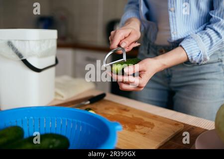 Hausfrau schält Gurkenhaut mit einem Schälwerkzeug in einer Hausküche. Weibliche Person bereitet zu Hause einen gesunden grünen Salat zu und recycelt Organi Stockfoto