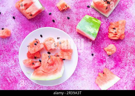 Wassermelonenscheiben auf einer weißen Platte auf einer rosafarbenen Oberfläche Stockfoto