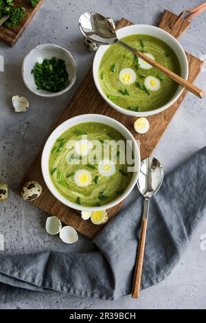 Traditionelle grüne Kräutersuppe mit Wachteleiern und Schnittlauch in Schüsseln auf einem Holzbrett Stockfoto